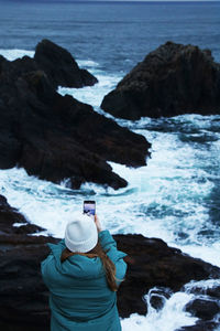 Rear view of woman in blue jacket looking at sea against sky