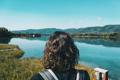 Girl sitting on the edge of banyoles lake on a sunny day with the landscape reflected in the water