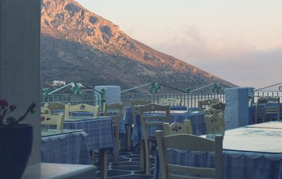 Empty chairs and tables at beach against sky