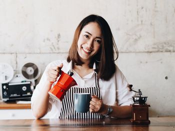 Portrait of smiling young woman pouring coffee in cup at counter