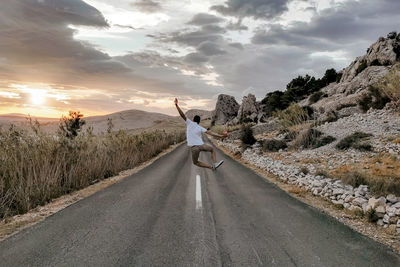 Rear view of man jumping in middle of open road. sumer, wanderlust, travel.