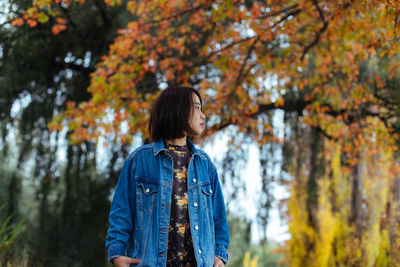 Mid adult woman looking away while standing against autumn trees