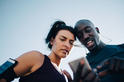 Low angle view of sportsman showing mobile phone to female athlete while standing outdoors