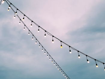 Low angle view of light bulbs hanging against sky