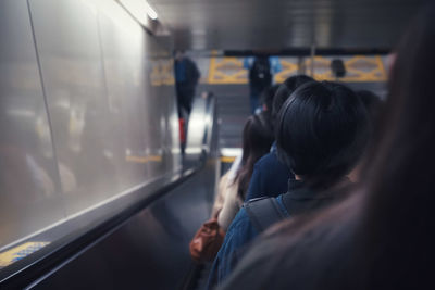 Rear view of people standing on escalator at subway station