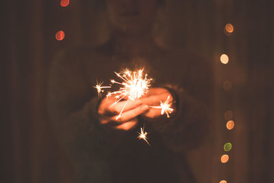 Midsection of woman holding lit sparkler at night