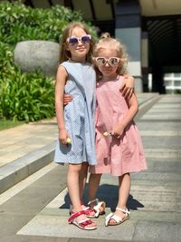 Full length portrait of sisters wearing sunglasses while standing on footpath