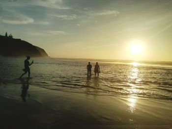 Silhouette people on beach against sky during sunset