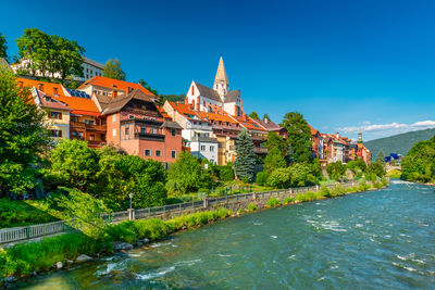 Buildings by river against clear blue sky