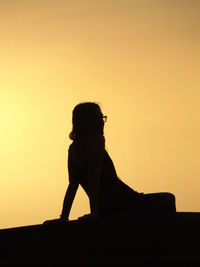 Silhouette woman photographing sculpture against clear sky