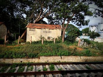 Abandoned house and trees by plants against sky