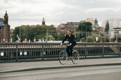 Businessman riding bicycle on street in city against sky