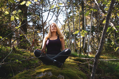 Beautiful woman meditating while sitting on land in forest