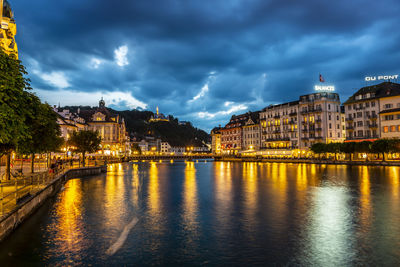 Illuminated buildings by river against sky in city