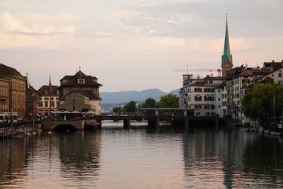 Bridge over river by buildings against sky in city