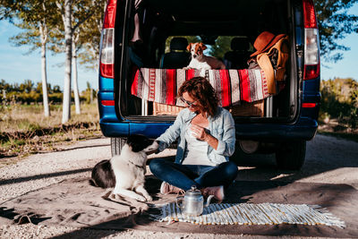 Woman holding mug while sitting with dog by camper trailer