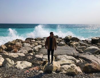 Full length of man standing on rock at beach against sky