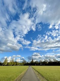 Empty road amidst field against sky