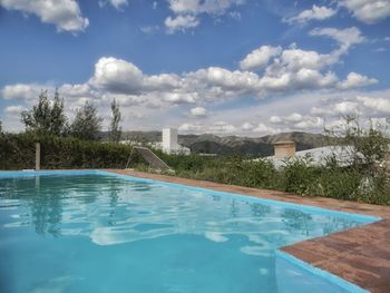 Swimming pool by trees against sky