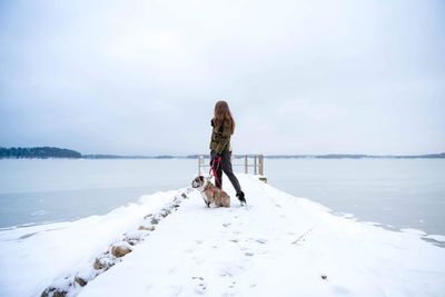 Woman with dog standing on snow against sea