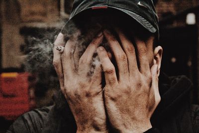 Close-up of man smoking cigarette while covering face with hands