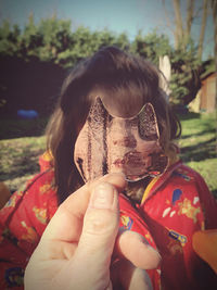 Cropped hand holding ice against girl face outdoors