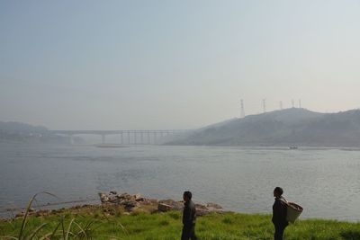 People standing on grass by river against sky