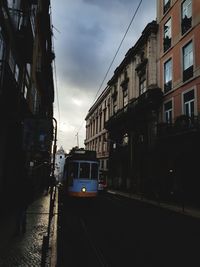 Train on street amidst buildings in city against sky