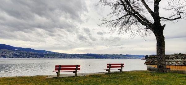 Bench on beach by lake against sky