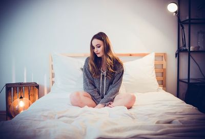 Young woman sitting on bed at home