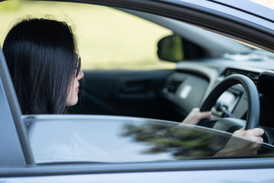 Side view of woman sitting in car seen through window