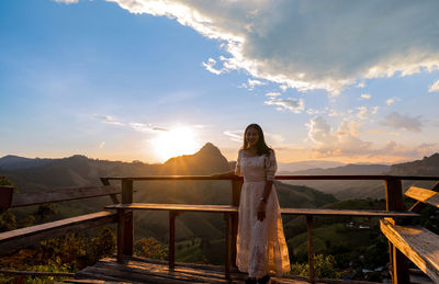 Rear view of woman walking on field against sky during sunset