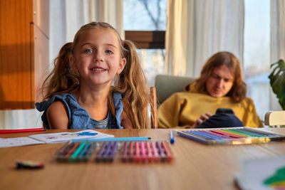 Girl takes markers from plastic box against man in room