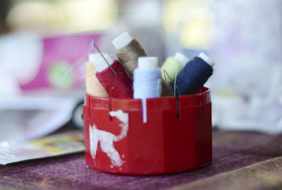 Close-up of spools and sewing needles in container on table