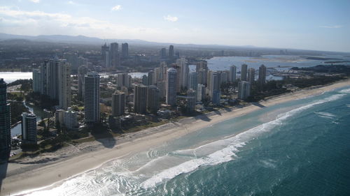 Aerial view of modern buildings by sea against sky