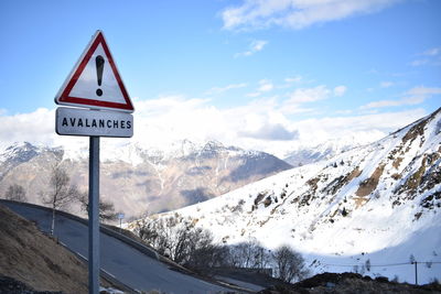 Road sign by snowcapped mountains against sky