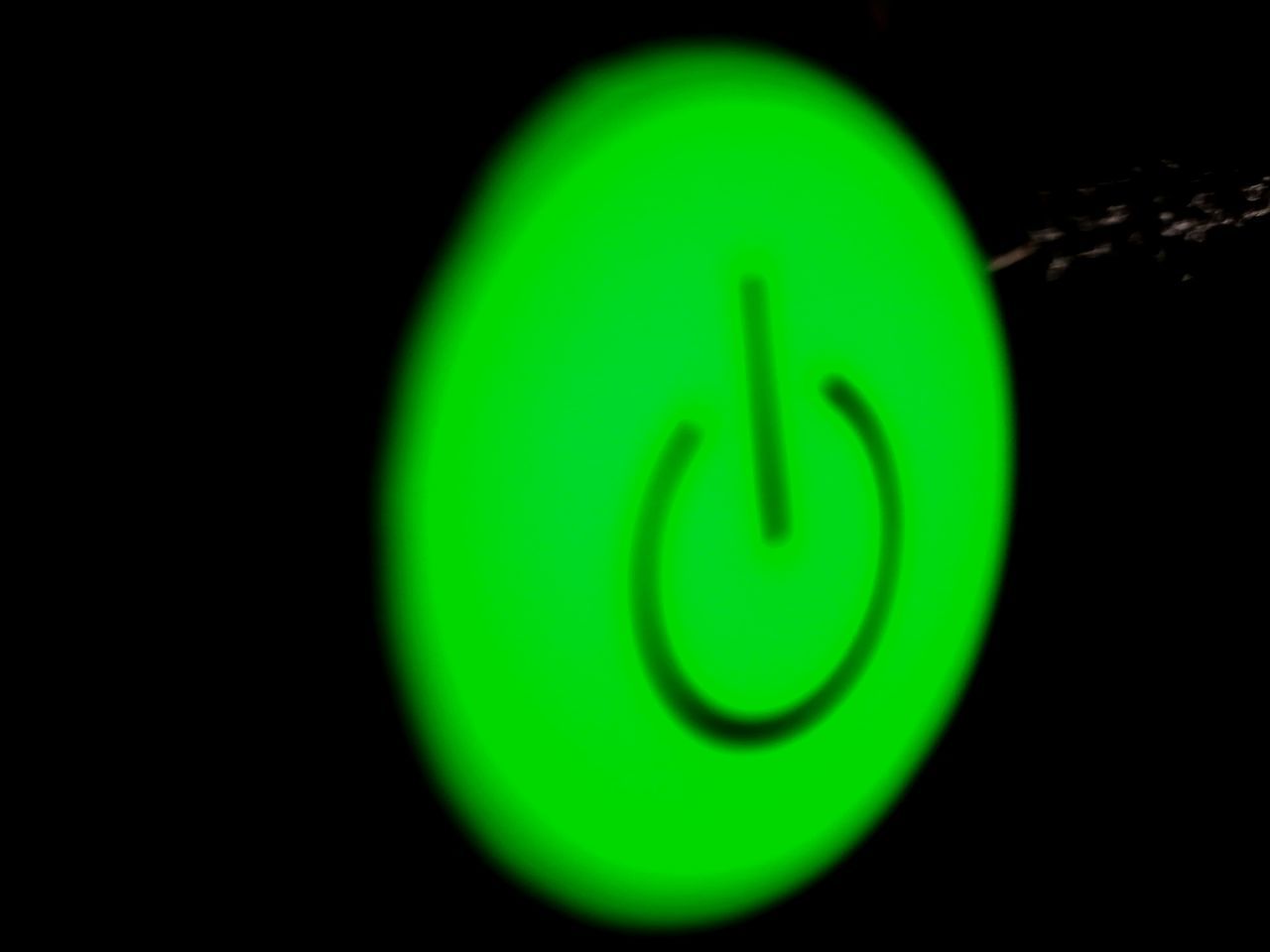 CLOSE-UP OF GREEN LIGHT AGAINST BLACK BACKGROUND AGAINST BLURRED WALL