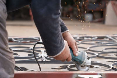 Man grinds metal fence with angle grinder. hands and tool close-up. side view