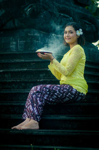 Portrait of woman holding mobile phone while sitting on staircase