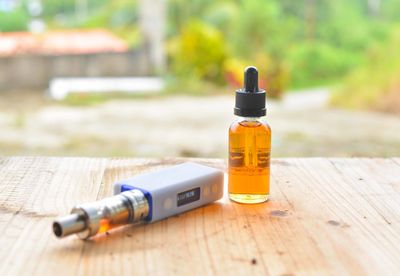 Essential oil in bottle by electronic cigarette on table