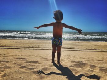 Full length of shirtless boy on beach against sky