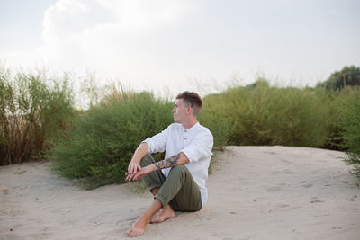 Young man using mobile phone while sitting on field against sky