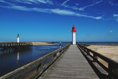 Pier leading towards lighthouse at beach during sunny day