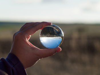 Close-up of hand holding crystal ball against sky