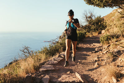 Full length of woman standing on rock by sea against sky