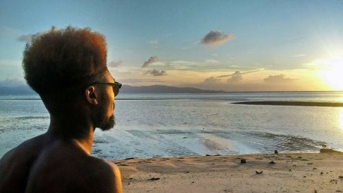 Man wearing sunglasses on beach against sky during sunset