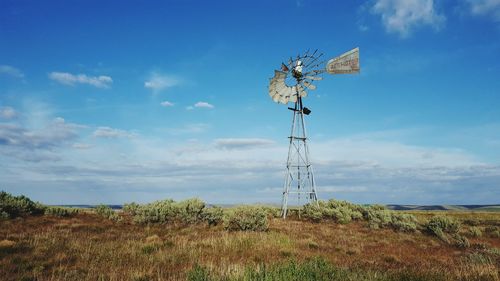 Low angle view of american-style windmill on field against cloudy blue sky