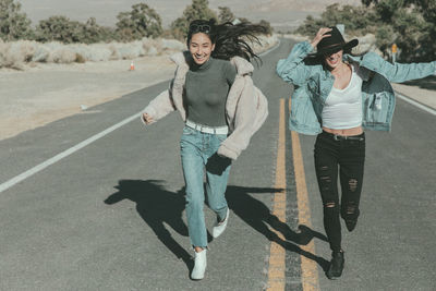 Full length of playful female friends running on road at desert during sunny day
