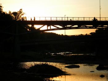 Silhouette bridge over river against sky during sunset