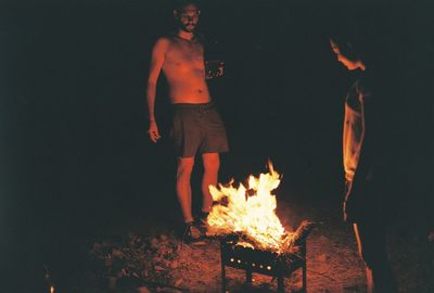 Friends standing by burning fire pit at night